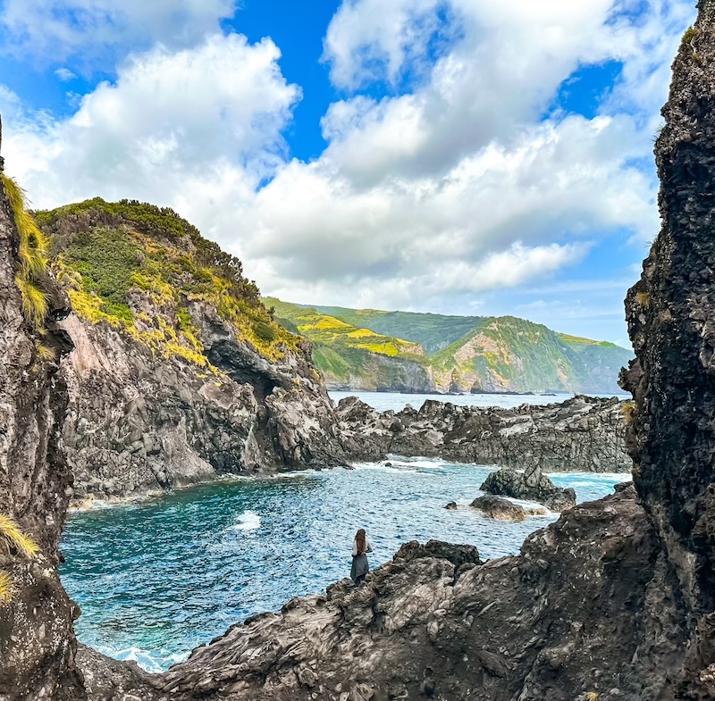 Elaina standing on a rock by the ocean looking out on the view in the Azores