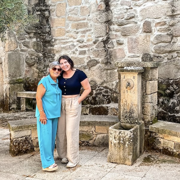 Elaina and her grandma standing next to an old, stone water fountain in the small village of Bobadela in northern Portugal