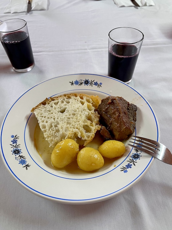 Typical Portuguese meal of potatoes, beef, and bread on a white ceramic plate with blue flower details and a glass of wine in the top right corner.