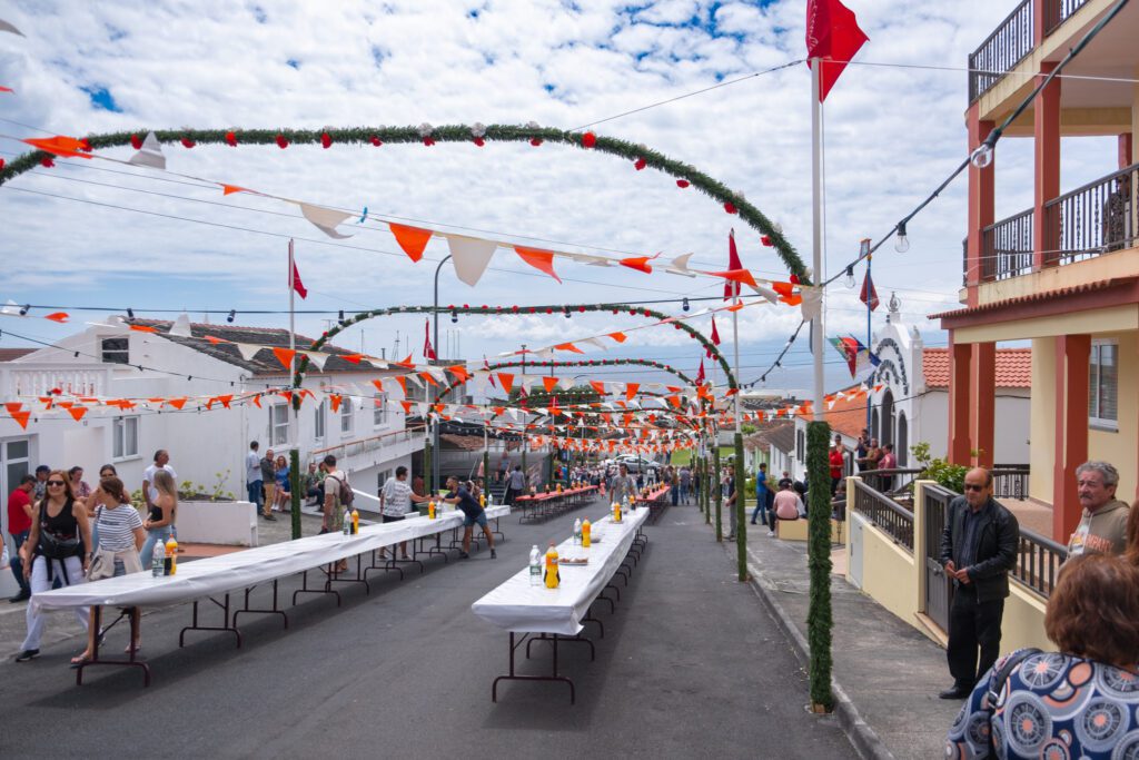 Tables line a long road in central Velas, Sao Jorge ready for the Azores festa about to begin. Red and white flags are tied between poles overhead, making a very festive view. 