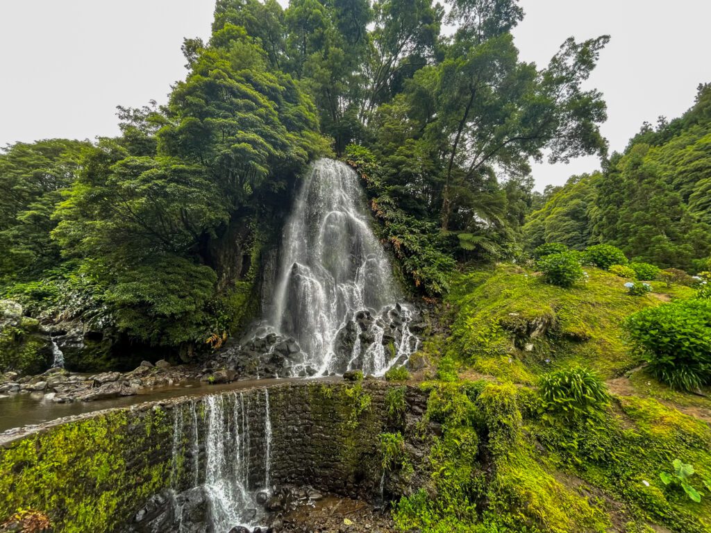 Top waterfall of Ribeira dos Caldeiros flows over the rocks and onto the walking path