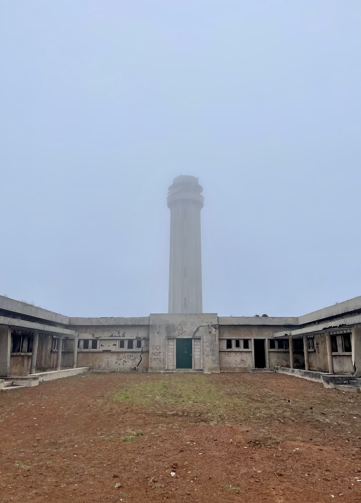 The abandoned lighthouse, Farol da Ponta dos Rosais, in Rosais, São Jorge, Azores. The lighthouse and rundown building has a haze of fog covering it. 